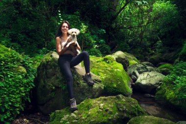 Genç bir kadın tropikal ormanda köpeğiyle poz veriyor. Güneşli bir günde yeşil ormandaki kadın ve evcil hayvan. Sürdürülebilir turizm kavramı. Amatlan, Meksika.