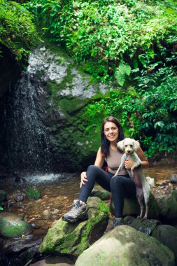 Genç bir kadın tropikal ormanda köpeğiyle poz veriyor. Güneşli bir günde yeşil ormandaki kadın ve evcil hayvan. Sürdürülebilir turizm kavramı. Amatlan, Meksika.