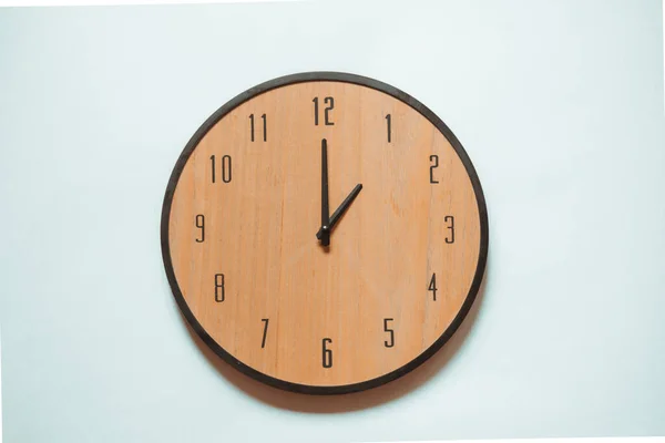 Wooden mechanical wall clock with black numerals and black hands showing one o\'clock.