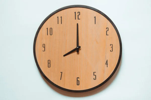 Wooden mechanical wall clock with black numerals and black hands showing eight o\'clock.