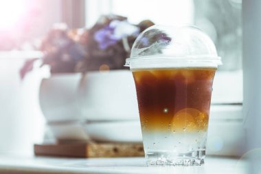 Plastik bardaktaki soğuk, çift katmanlı espresso toniği bir kahve dükkanının pencere eşiğinde durur..