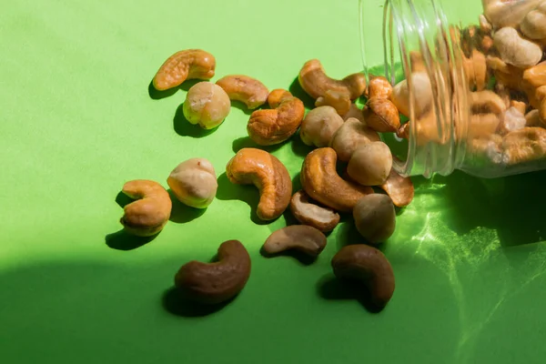 Scattered Nuts Glass Jar Green Background Hazelnuts Cashews — Fotografia de Stock