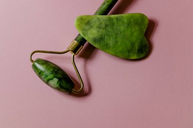 Yüz masajı için doğal taştan yapılmış bir masaj seti. Pembe arka planda Jade silindiri ve scruber..