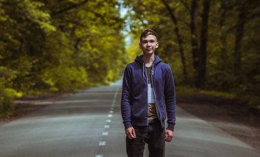 Genç bir adam ormanda yolun ortasında yavaşça yürüyor..