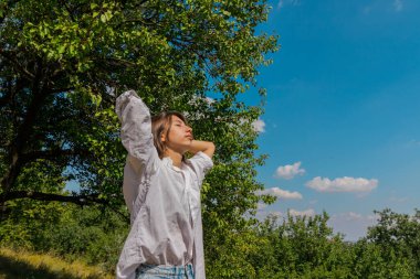  Gözleri kapalı beyaz gömlekli bir kız, temiz havanın ve doğanın tadını çıkarıyor..