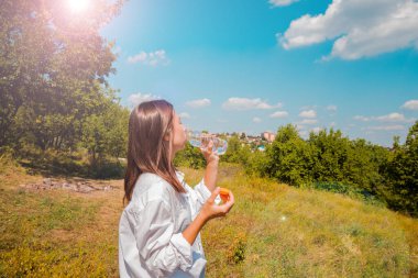 Bir kız yeşil bir çayırın arka planında su içiyor..
