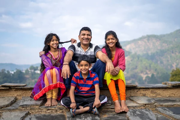 Indian Father sitting with his kids smiling while looking into the camera. Happy family concept.