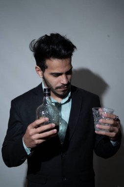 Takım elbiseli, elinde rom şişesi olan ve cama dik dik bakan klas bir genç. Ofis partisi konsepti.