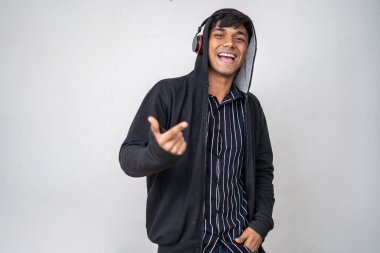 Kulaklıklı, siyah kapüşonlu müzik dinleyen genç yakışıklı bir adam. Bir eli cebinde, beyaz arka planda duruyor.