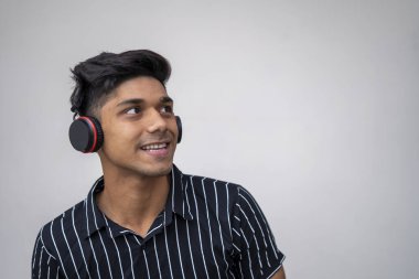Genç yakışıklı adam, beyaz arka planda kulaklıkla müzik dinliyor..