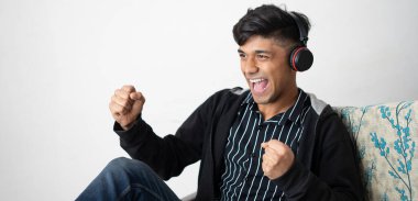 Kulaklıklı Asyalı bir adam siyah ceketli. Elinde olumlu bir jest, gülümsüyor ve başarı için seviniyor..