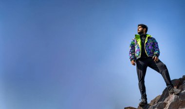 Uçurumun tepesinde kar yelekli ve eşofmanlı genç bir çocuğun resmi. Zevk ve özgürlük kavramı.