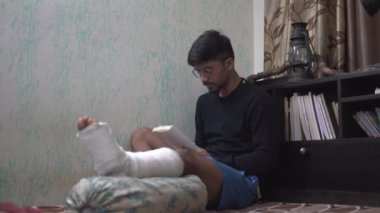 Yatakta otururken kitap okuyan kırık bacaklı bir adamın yanına..