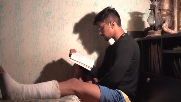 Мальчик Индеец Читает Книгу Темноте Настольной Лампой Сидя Кровати Сломанной — стоковое видео