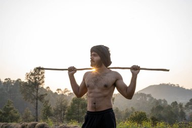 Issız bir yerde elinde sopayla yürüyen genç Hintli çiftçi. Yağmur ve su sıkıntısı nedeniyle ekinler büyümüyor.