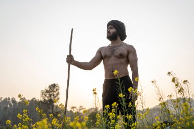 Issız bir yerde elinde sopayla yürüyen genç Hintli çiftçi. Yağmur ve su sıkıntısı nedeniyle ekinler büyümüyor.