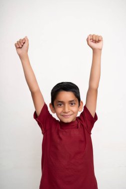 Genç Hintli çocuk kollarını havaya kaldırarak neşeli bir ifade sergiliyor beyaz izole bir arka planda duruyor..