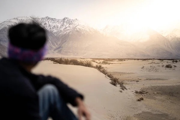 A lost man sitting alone on the top of a mountain and looking at the hills around during a very cloudy winter day. He is feeling lonely. The man is not in focus