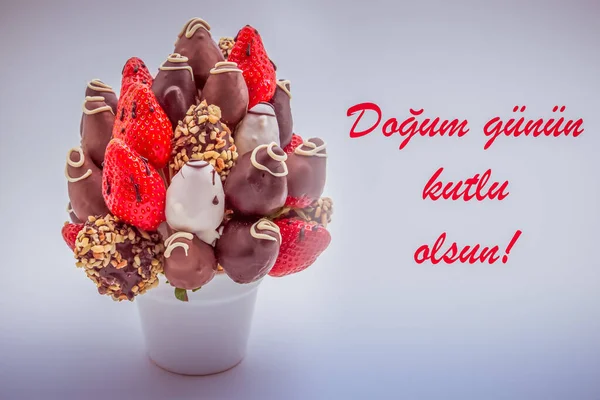 ドグム グヌン クートルル サンを読む赤い文字でトルコ語で幸せな誕生日の挨拶カード 食用の花の束 白に隔離されたチョコレート浸したイチゴの配置 — ストック写真