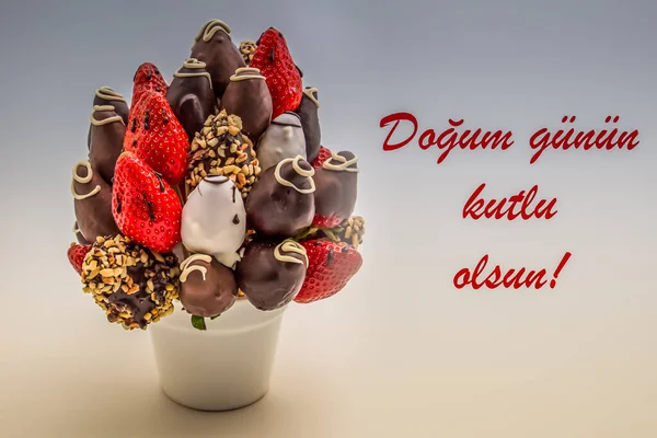 ドグム グヌン クートルル サンを読む赤い文字でトルコ語で幸せな誕生日の挨拶カード 食用の花の束 白に隔離されたチョコレート浸したイチゴの配置 — ストック写真