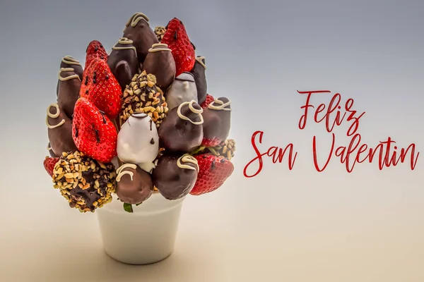 Üzerinde Feliz San Valentin yazan kırmızı harflerle İspanyolca Sevgililer Günü tebrik kartın, bir demet yenilebilir çiçek, beyaz üzerine izole edilmiş çikolatalı çilek düzenlemen kutlu olsun.