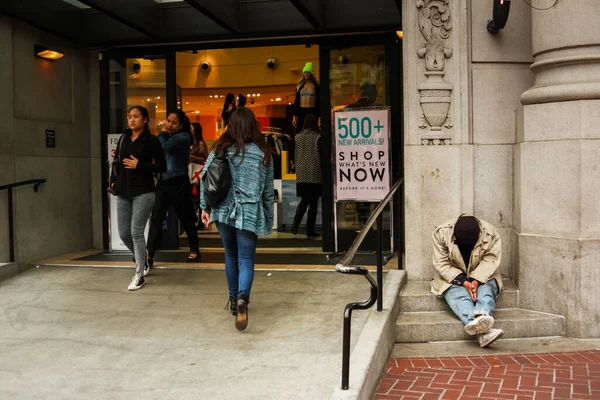 San Francisco, Kaliforniya / Amerika Birleşik Devletleri - 27 Mayıs 2013: İnsanlar San Francisco, Kaliforniya, Amerika Birleşik Devletleri 'nde yürürken lüks bir alışveriş merkezinin önünde oturan evsiz adam