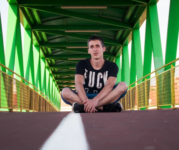photo session on a green bridge near madrid with our model George wearing a black t-shirt and short jeans