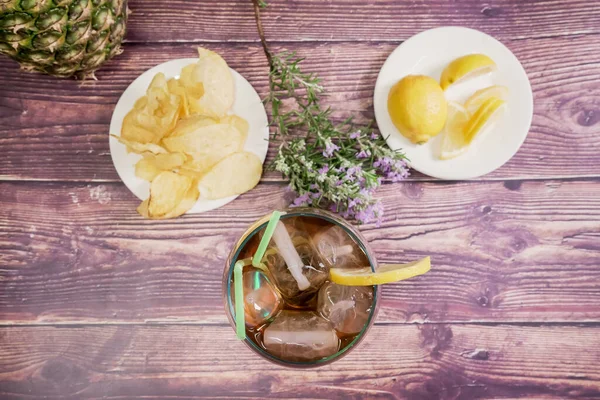 Cips, limon ve ahşap arka planlı biberiye çiçeği manzaralı viski bardağı.