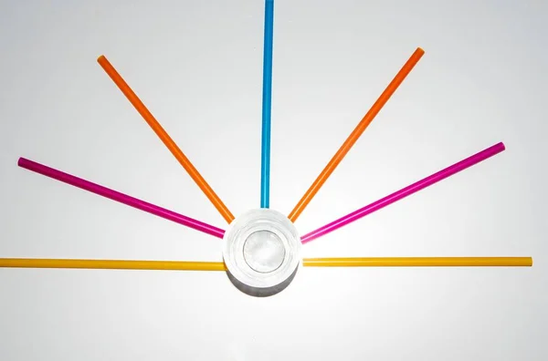 Güneş şeklini alan renkli pipetler. Ortasında boş bir bardak var. Üst görünüm.