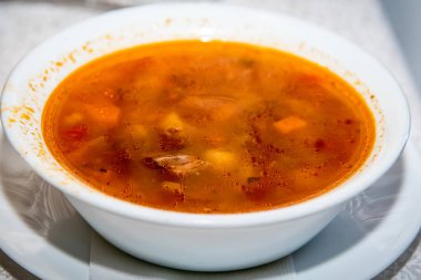 Beyaz tabakta et çorbası, aynı renkte bir masa örtüsü ile bir restoran masasında.