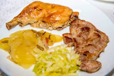 Beyaz tabakta patates ve lahana salatası ile tavuk ve domuz bifteği.