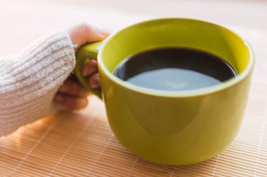 Süt renginde bir kazak giymiş bir el kahve ile yeşil bir fincanın sapının yanında