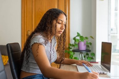 Kız, evden bilgisayarla uğraşırken oturma odasındaki masada oturan bir kağıt parçasına notlar yazıyor..