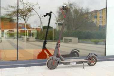 Gri elektrikli scooter 'ın görüntüsü onları bir karedeki büyük bir cama yansıtıyor.