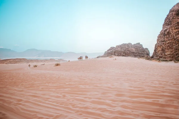 Люди Верблюдах Проходят Песчаные Дюны Пустыне Которая Окружена Каменными Камнями — стоковое фото