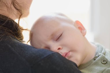 Annesinin omzunda uyuyan küçük çocuk.