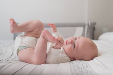 Beyaz çarşaflı, kocaman bir yatakta uyuyan sevimli bir bebek.