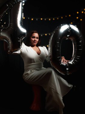 Bankta oturan bir kadın elinde balonlarla fotoğraf için poz veriyor ve beyaz giyiyordu.