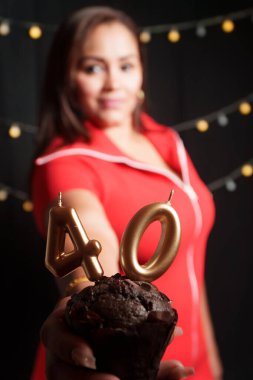 Siyah arkaplan ve elinde 40 numaralı pasta olan kırmızı elbiseli bir kadın odak dışı ve 40 numara odaklı.
