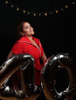 Bir kadın üzerinde 40 yazan iki gümüş balonun önünde duruyor. Kırmızı bir elbise giyiyor.