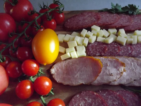 Нарезка копченой колбасы из четырех сортов с сыром и красными и желтыми помидорами и помидорами черри — стоковое фото