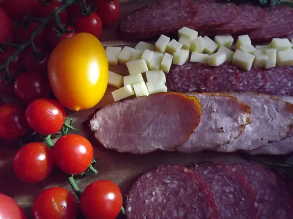 Нарезка копченой колбасы из четырех сортов с сыром и красными и желтыми помидорами и помидорами черри — стоковое фото
