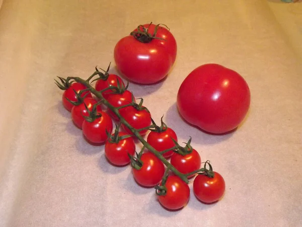 Dois tomates grandes e tomates de cereja em ramos fecham-se em um contexto bege — Fotografia de Stock