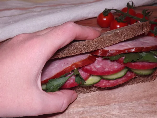 Farklı türde sosis ve sebzeli bir sandviçi tutarken. — Stok fotoğraf