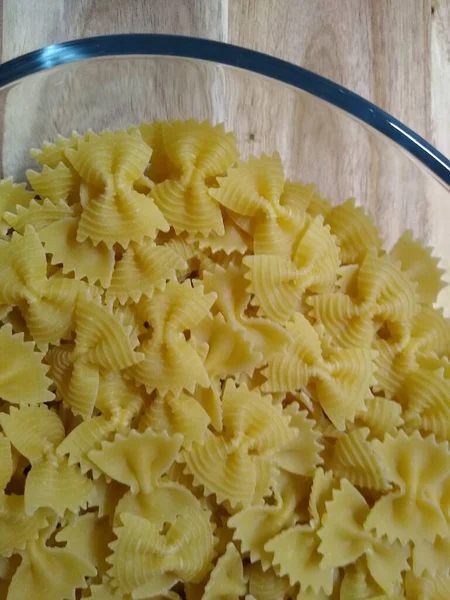 Pasta in the form of bows in a glass container on a wooden background — Stock Photo, Image