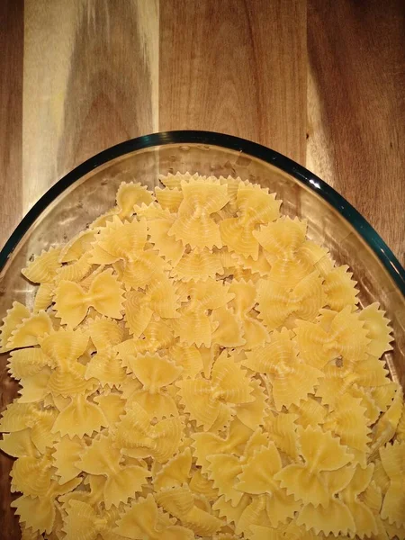 Pasta in Form von Schleifen in einem Glasbehälter auf einem hölzernen Hintergrund — Stockfoto