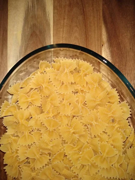 Pasta in the form of bows in a glass container on a wooden background — Stock Photo, Image