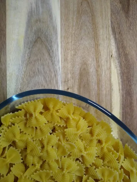 Pasta in the form of bows in a glass container on a wooden background — Stock Photo, Image