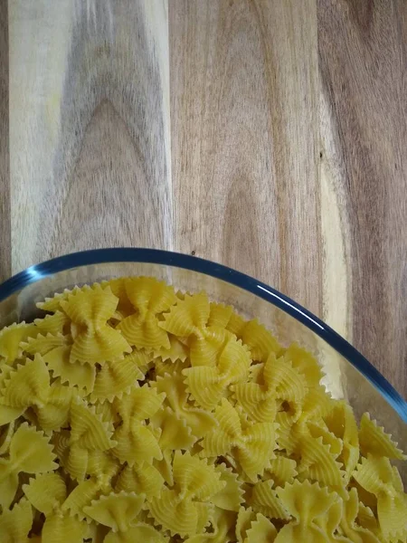 Pasta in de vorm van strikken in een glazen container op een houten ondergrond — Stockfoto