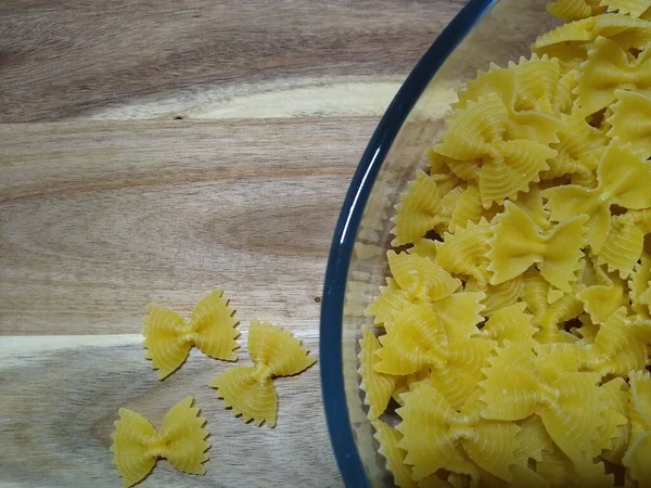 Macarrão na forma de arcos em um recipiente de vidro em um fundo de madeira — Fotografia de Stock